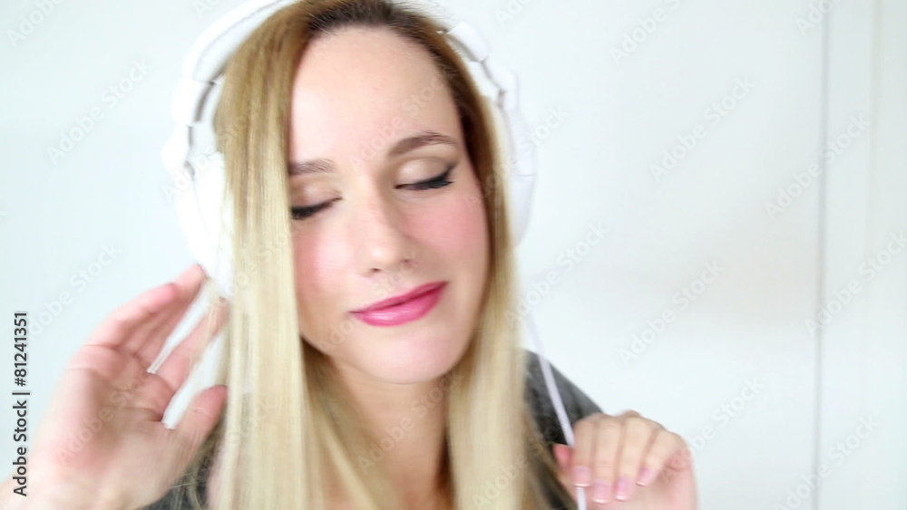 Beautiful young blond woman dancing with white headphones in white bright background Beautiful young blond woman dancing with white headphones in white bright background
