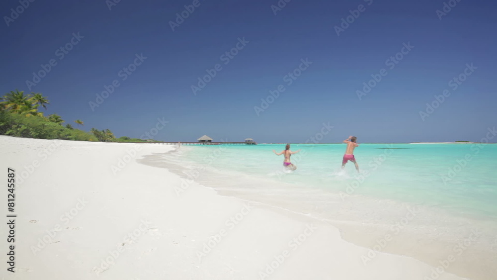 couple running across sandy beach into tropical lagoon on sunny vacation day with clear blue sky couple running across sandy beach into tropical lagoon on sunny vacation day with clear blue sky