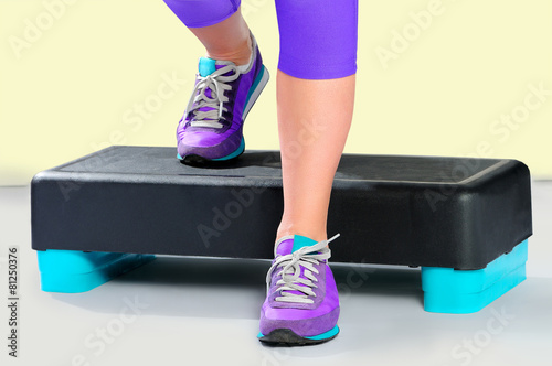 Female feet in violet sneakers on fitness aerobic stepper.