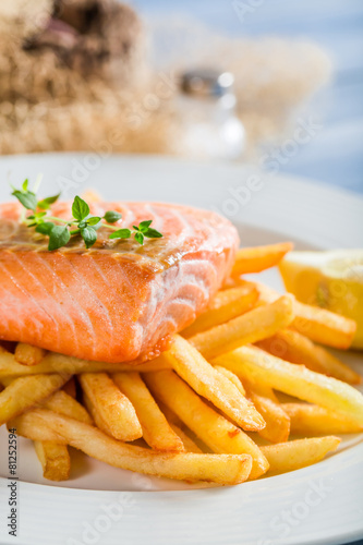 Hot french fries with salmon served on plate with lemon