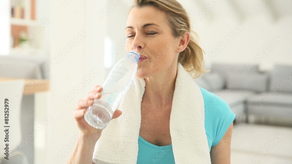 Mature woman drinking water from bottle after exercising Mature woman drinking water from bottle after exercising