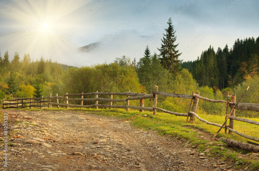 Landscape in a mountain valley: road and wooden fence.