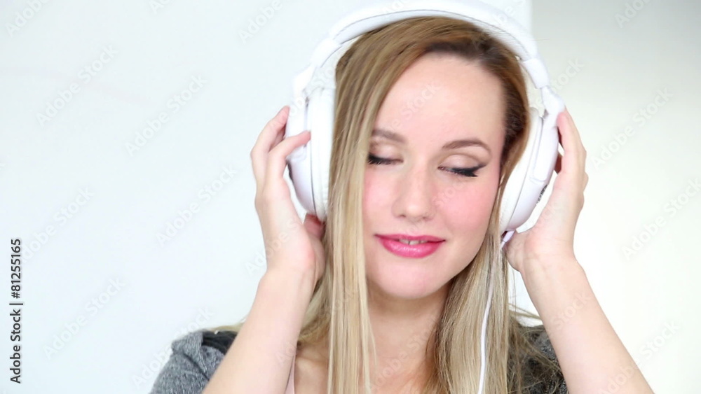 Beautiful young blond woman dancing with white headphones in white bright background Beautiful young blond woman dancing with white headphones in white bright background