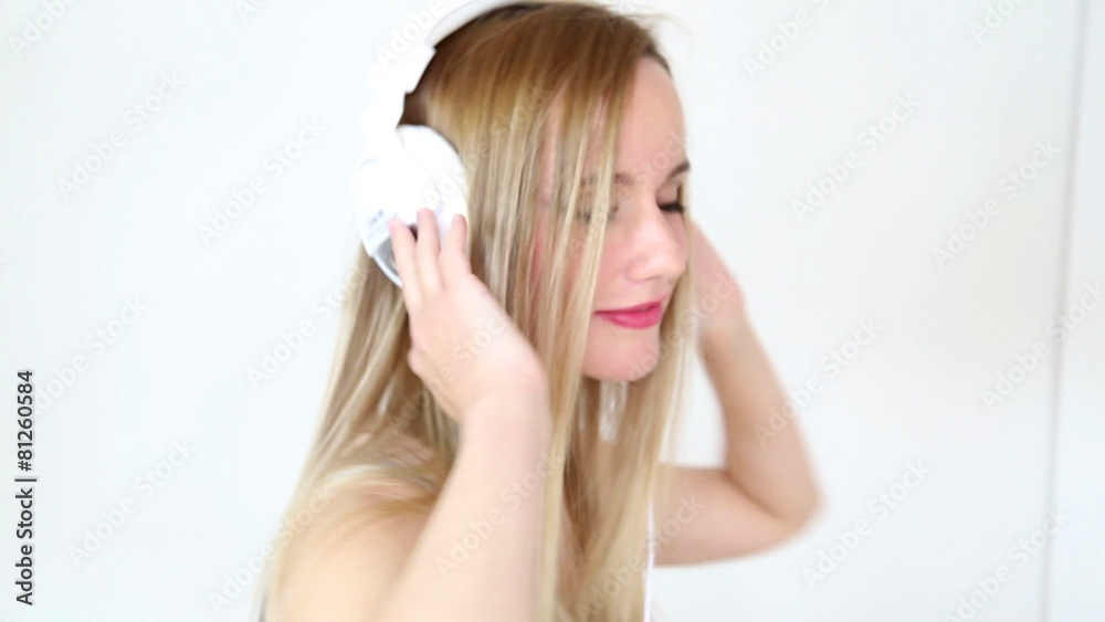 Beautiful young blond woman dancing with white headphones in white bright background Beautiful young blond woman dancing with white headphones in white bright background