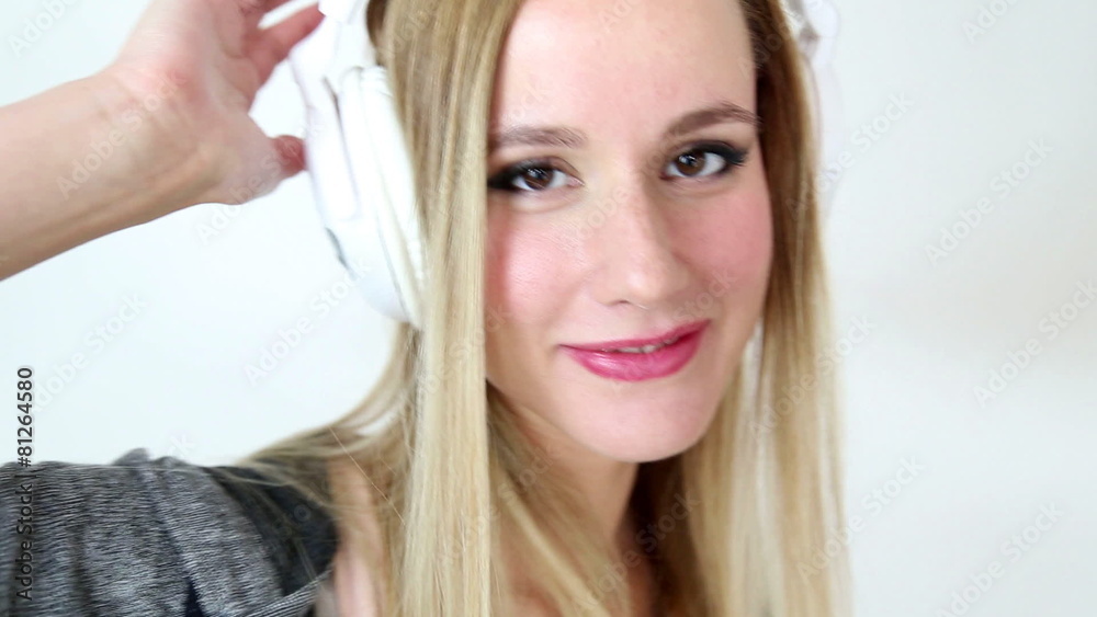 Beautiful young blond woman dancing with white headphones in white bright background Beautiful young blond woman dancing with white headphones in white bright background