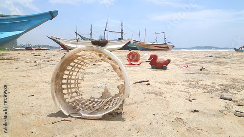 WELIGAMA, SRI LANKA - MARCH 2014: Trash washed up on shore in front of wooden fishing boast on beach. photo