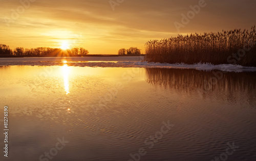 Winter landscape with river, reeds and sunset sky. Beautiful win