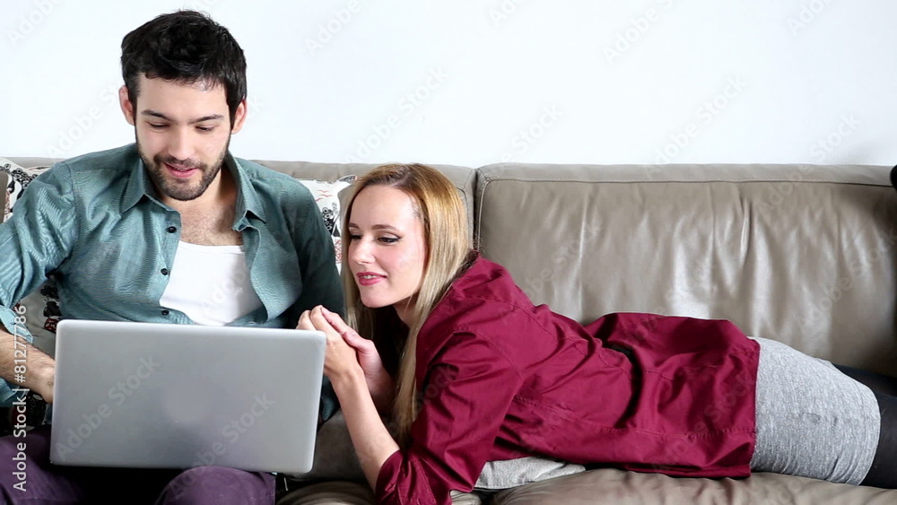 Happy couple on comfortable couch surfing on laptop in living room Happy couple on comfortable couch surfing on laptop in living room