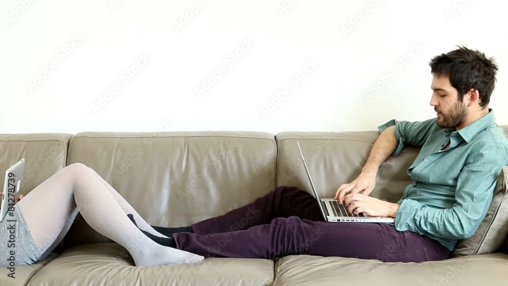 Man typing on computer speaking to pretty lady on couch Man typing on computer speaking to pretty lady on couch