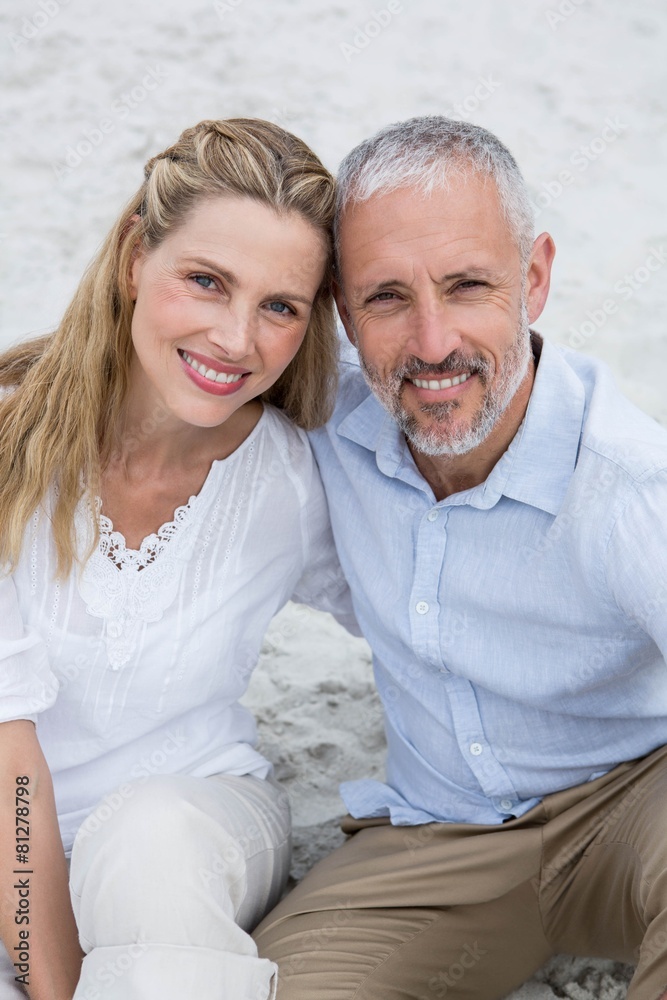 Happy couple sitting on the sand and looking at the camera