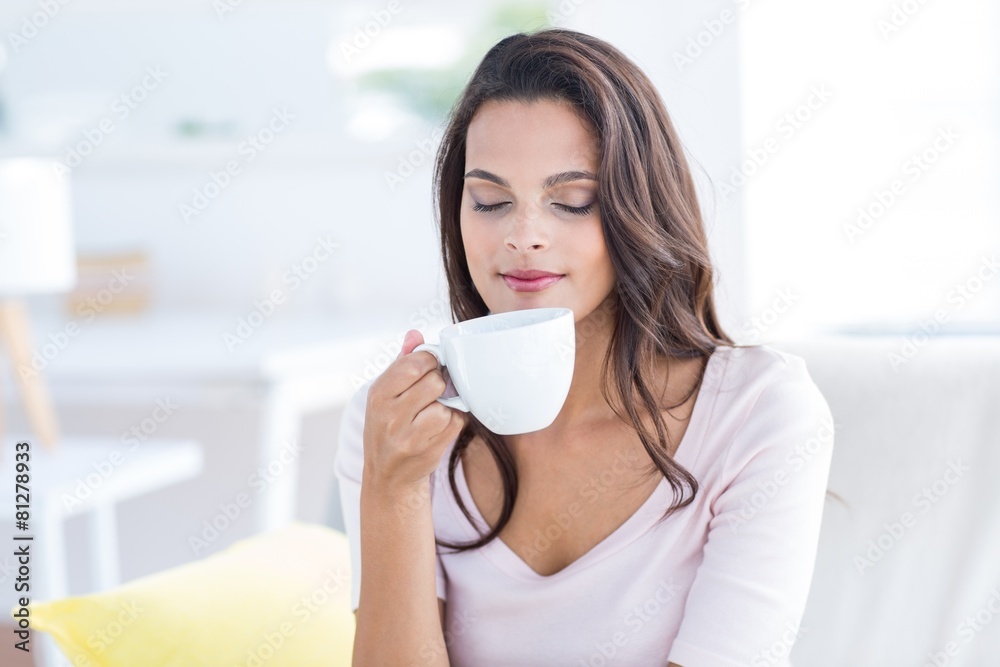 Smiling beautiful brunette relaxing on the couch and holding mug Smiling beautiful brunette relaxing on the couch and holding mug