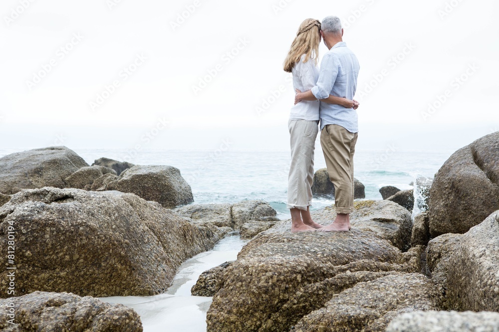Happy couple standing on the rock and looking at the sea Happy couple standing on the rock and looking at the sea