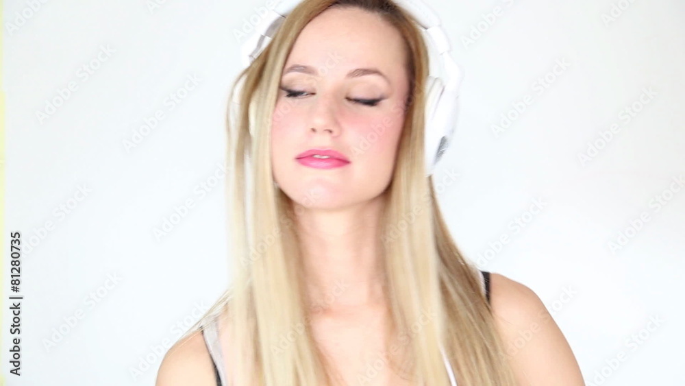 Beautiful young blond woman dancing with white headphones in white bright background Beautiful young blond woman dancing with white headphones in white bright background