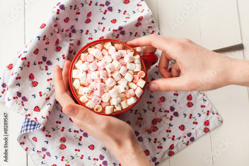 Hands holding hot chocolate with marshmallows in cup