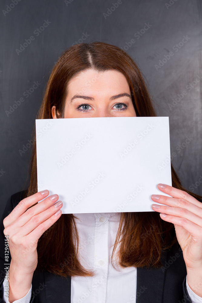 Junge Dame hält weißes Schild vor Mund / Schaut auf Betrachter Junge Dame hält weißes Schild vor Mund / Schaut auf Betrachter