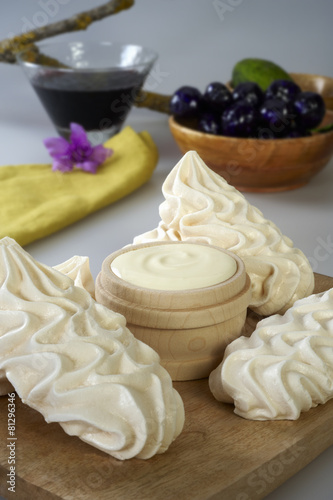 Wooden board with meringues and a bowl of cream.