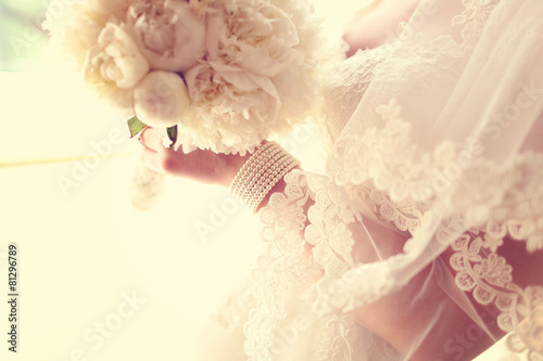 Hands of a bride holding white peonies bouquet