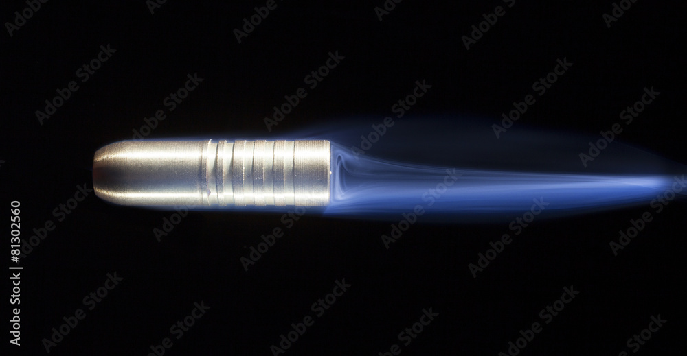 Flying copper bullet on a black background with blue smoker streaking behind. Flying copper bullet on a black background with blue smoker streaking behind.