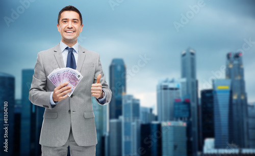 smiling businessman with money showing thumbs up