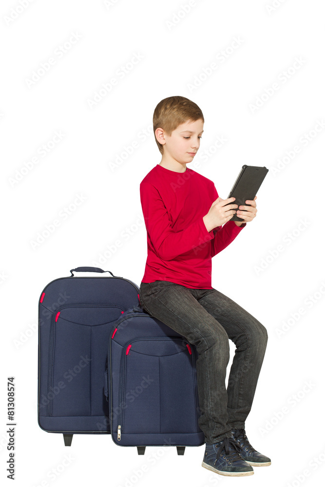 Boy sitting on travel bags with tablet pc isolated on white Boy sitting on travel bags with tablet pc isolated on white