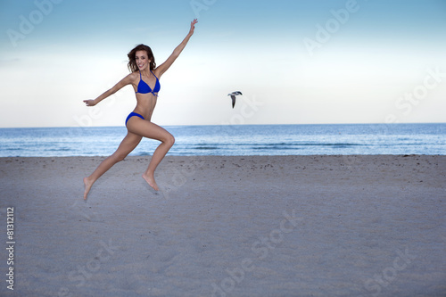 Young cheerful woman in bikini jumping on the beach.