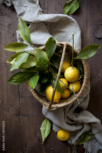 fresh lemons with leaves on straw basket on wooden table