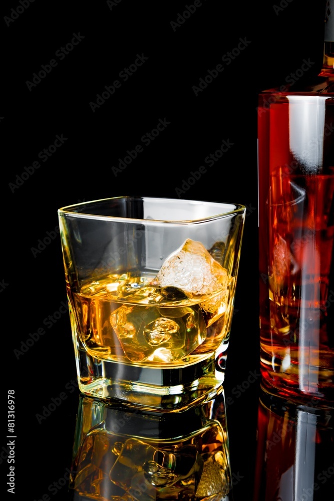 whiskey with ice in glass near bottle on black background