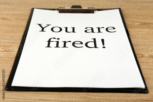Message You're Fired on clipboard on wooden table, closeup