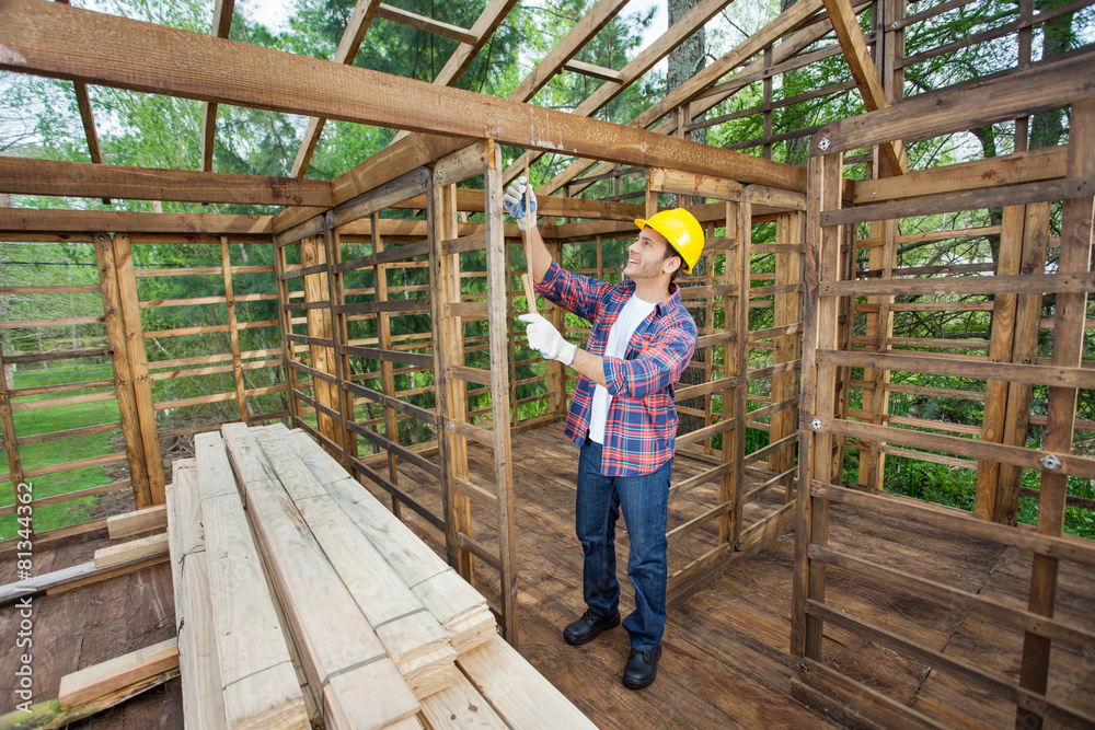 Worker Taking Measurements In Timber Cabin