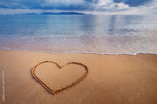 A drawing of a heart on a yellow sand at a beautiful seascape ba