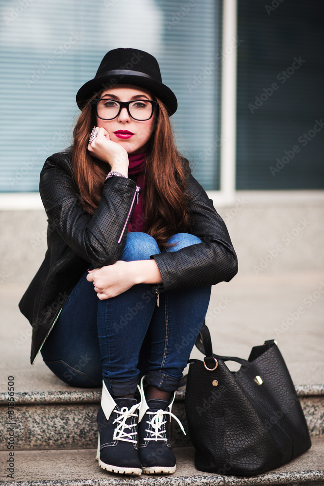 Fototapeta premium the stylish city girl in sunglasses sits on steps