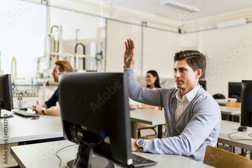 Young handsome man sitting in front of a computer raising hand © NDABCREATIVITY