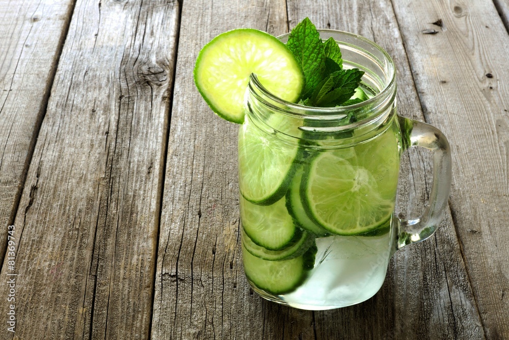 Detox water with lime and cucumbers in a mason jar against wood