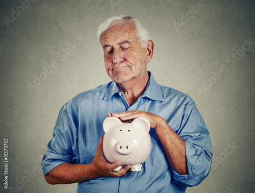 Slika na platnu Senior man holding piggy bank on gray wall background