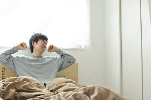 ベッドの上で眠そうにしているパジャマ姿の男性