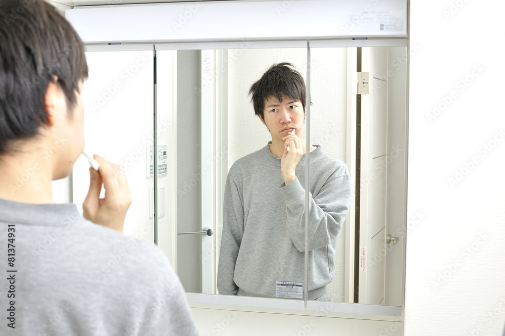 Fototapeta premium 朝起きて洗面所の鏡の前で歯を磨く日本人男性
