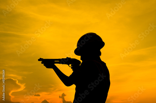 Silhouette boy holding shotgun with sun set.
