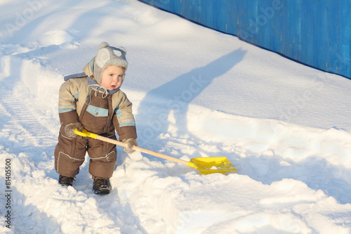Little handsome boy wearing jumpsuit holds shovel on snow 