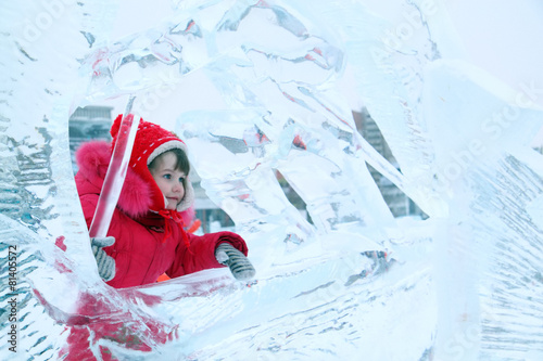 Little happy girl in red warm clothes plays in ice sculpture 