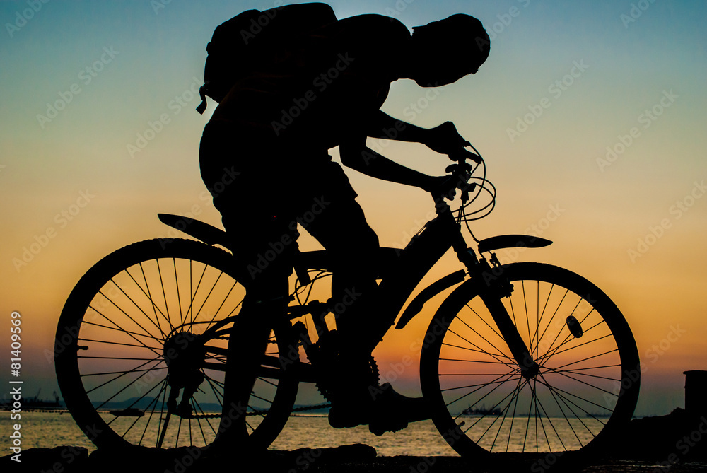 Fototapeta premium Silhouette of backpacker ride mountain bike on bridge beside sea