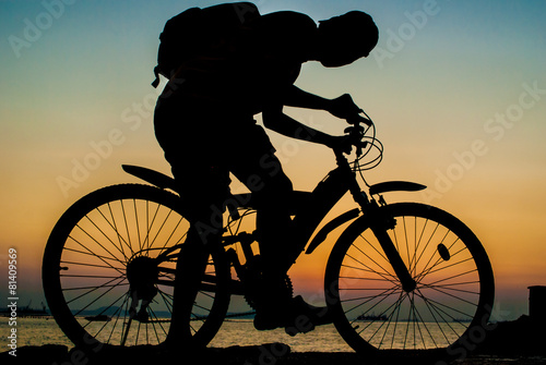 Silhouette of backpacker ride mountain bike on bridge beside sea