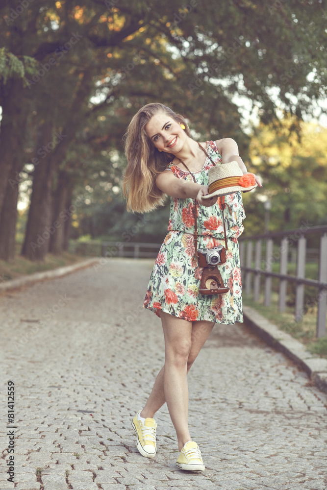 Happy young woman in a summer dress holding hat in hands