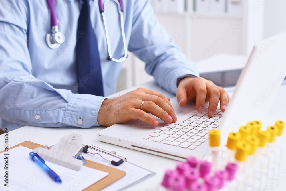 Male doctor using a laptop, sitting at his desk Male doctor using a laptop, sitting at his desk