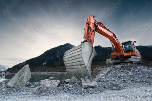 heavy organge excavator with shovel standing on hill with rocks photo