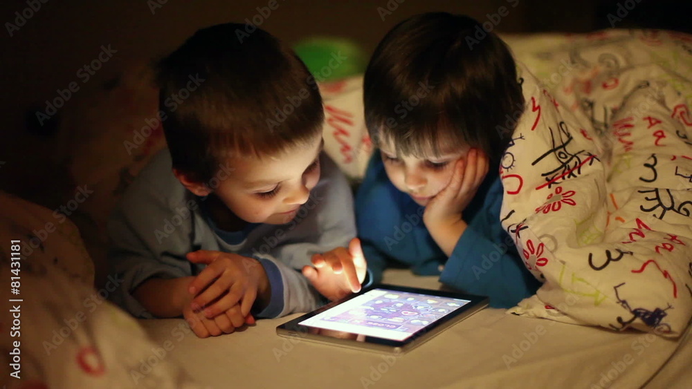 Little brothers playing on tablet in bed at night Little brothers playing on tablet in bed at night