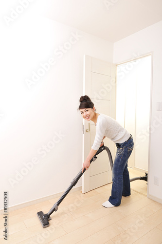 新築の白い部屋に掃除機をかけているアジア人女性