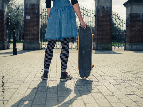 Young woman standing at gates of park with skateboard