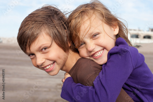 Foto Happy elementary-age boy giving piggyback ride to laughing girl outdoors on a sunny summer day