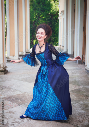 Obraz na plátně Beautiful young woman in blue medieval dress doing curtsey