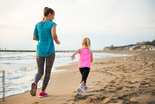 Healthy mother and baby girl running on beach. rear view